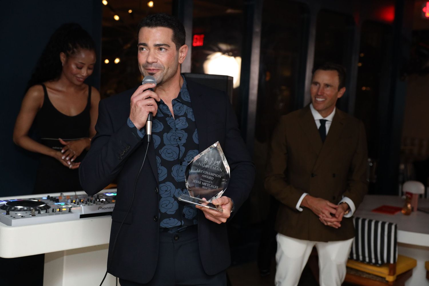 A person holds a trophy award while speaking into a microphone at an evening event.