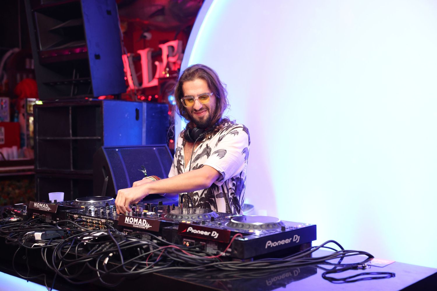 DJ performing at a nightclub with professional equipment and mixing deck illuminated by blue and red lighting.