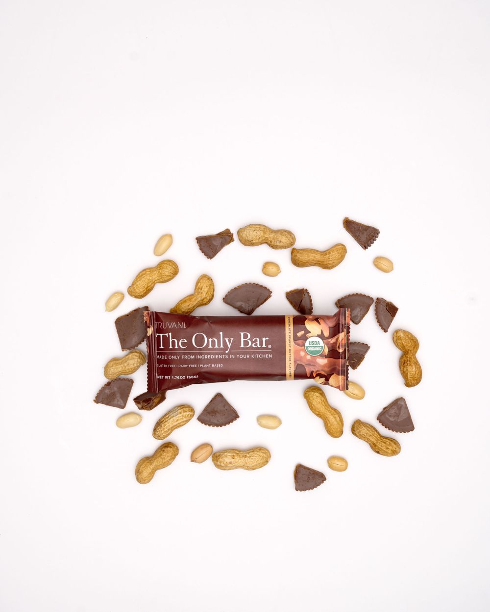 Chocolate chunks and peanuts arranged around a protein bar on white background.