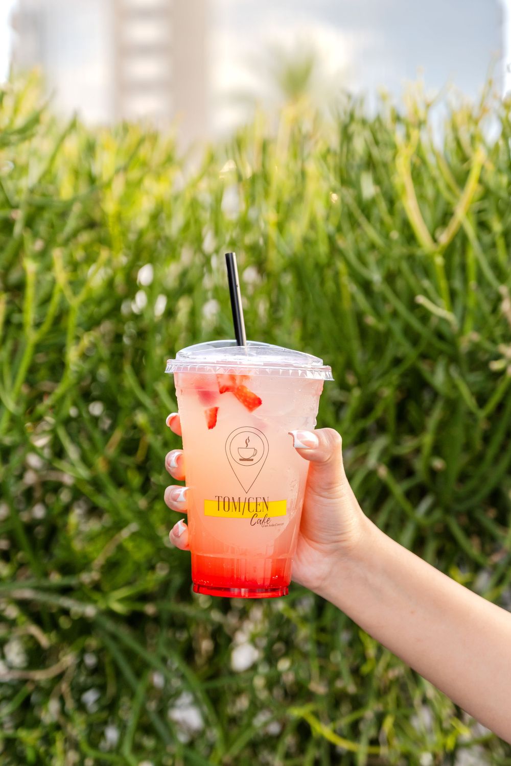 Hand holding a colorful gradient iced drink with red garnish against green foliage.