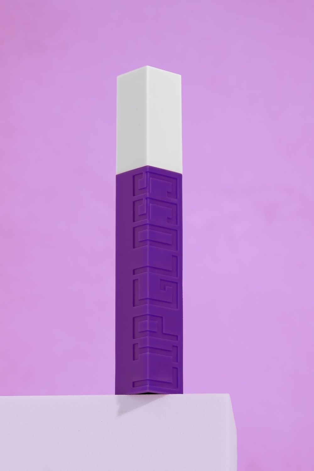Minimal product photography of purple and white geometric cosmetic container against purple background.