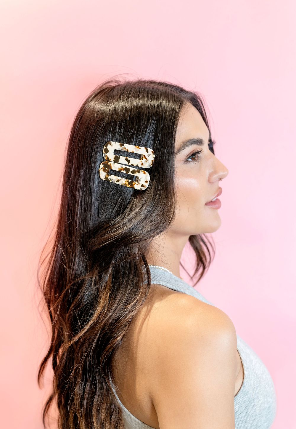 Side profile portrait with decorative pearl hair clip against pink background.