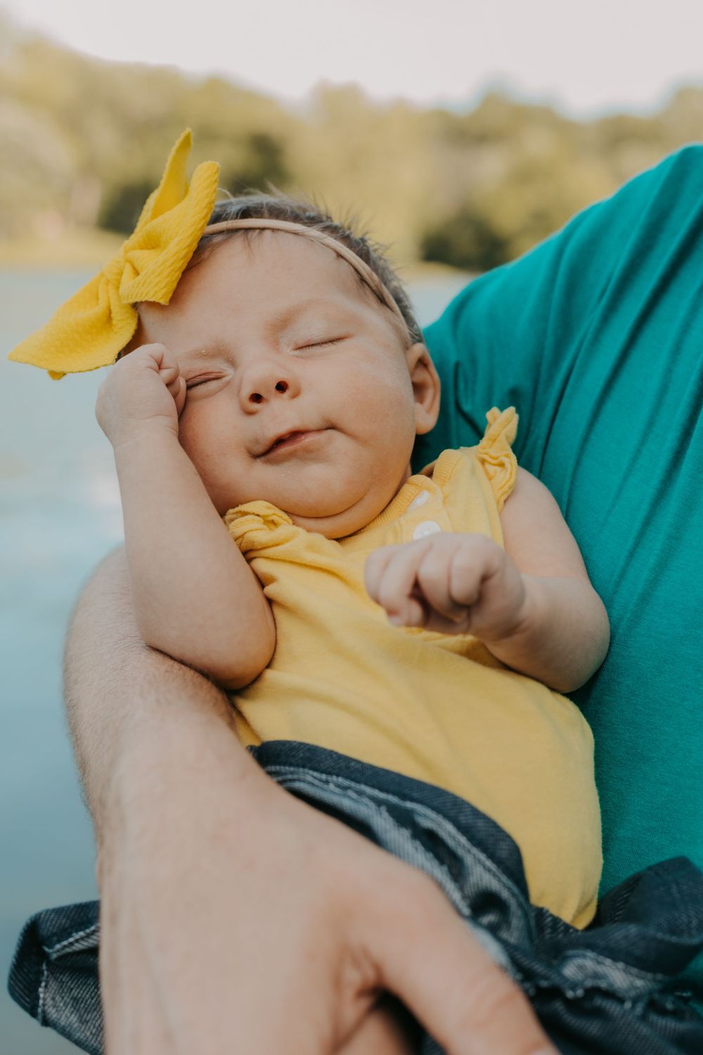 Sleeping baby in yellow outfit with matching bow resting on caregiver.