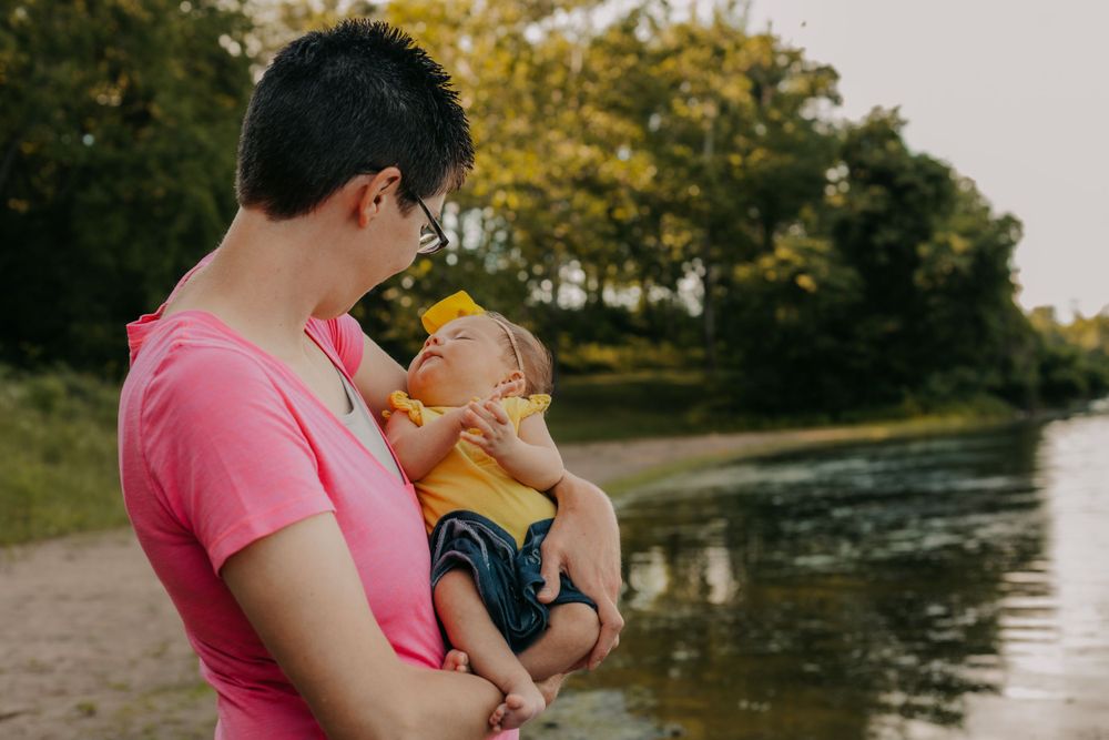 Sunset portrait by lake of caregiver holding infant in yellow outfit.