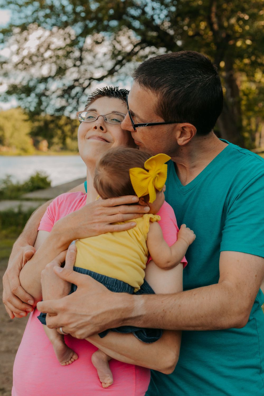 Tender family moment outdoors with infant wearing yellow bow.