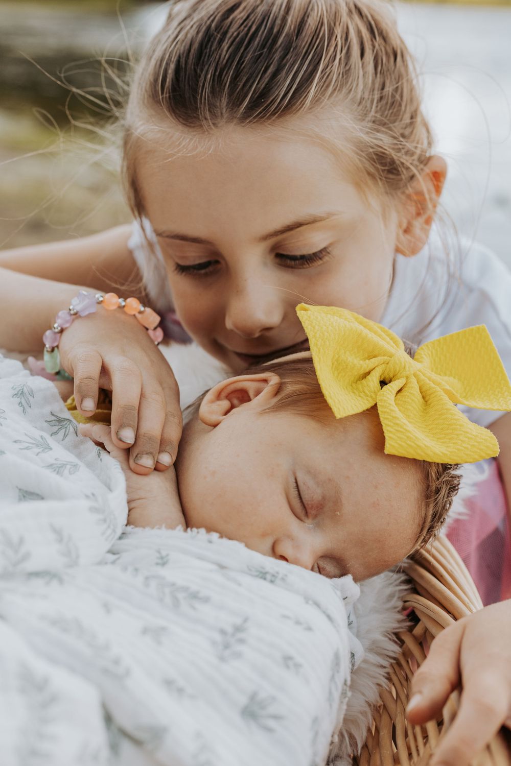 Sweet moment captured with sleeping baby in white blanket wearing yellow hair bow.