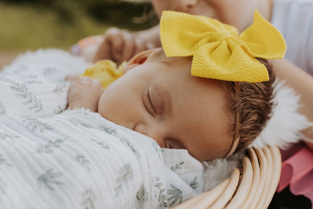 Peaceful sleeping baby adorned with yellow bow on white textured blanket.