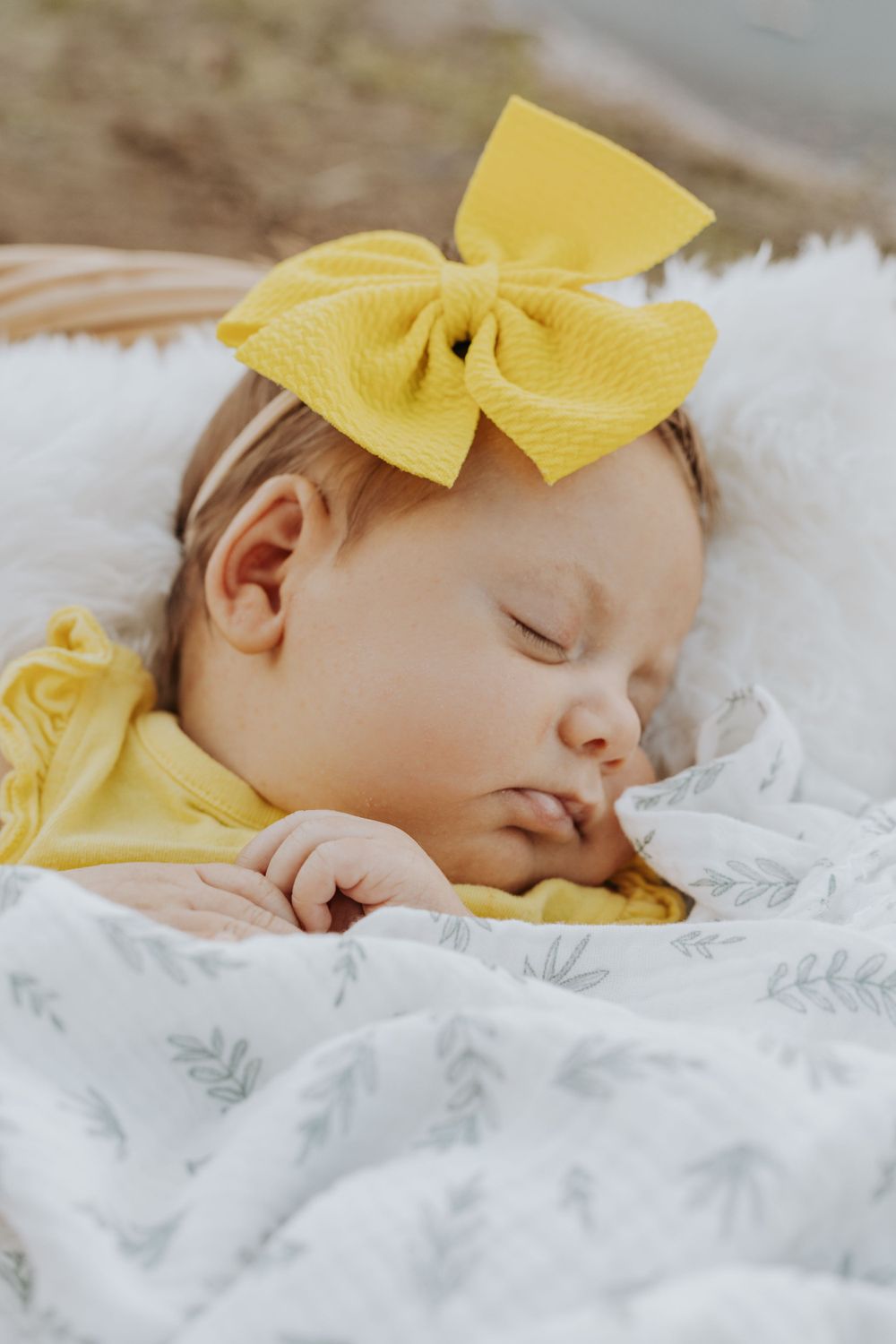 Sleeping baby in white floral blanket wearing bright yellow bow headband.