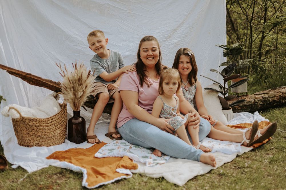 A family enjoys a picnic on a white blanket with decorative pampas grass and woven basket.