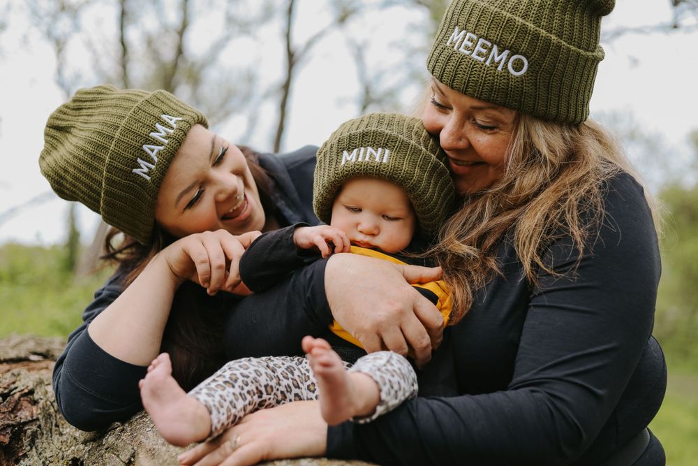 Family shares tender moment outdoors while wearing matching olive green knit beanies.
