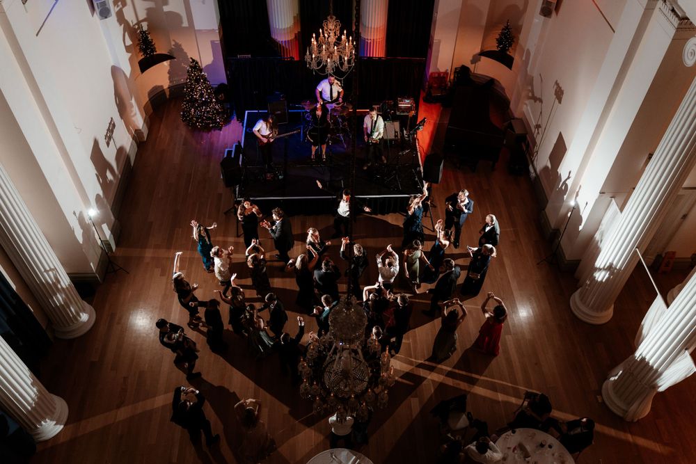Wedding reception venue with elegant lighting and guests dancing on a dark dance floor.
