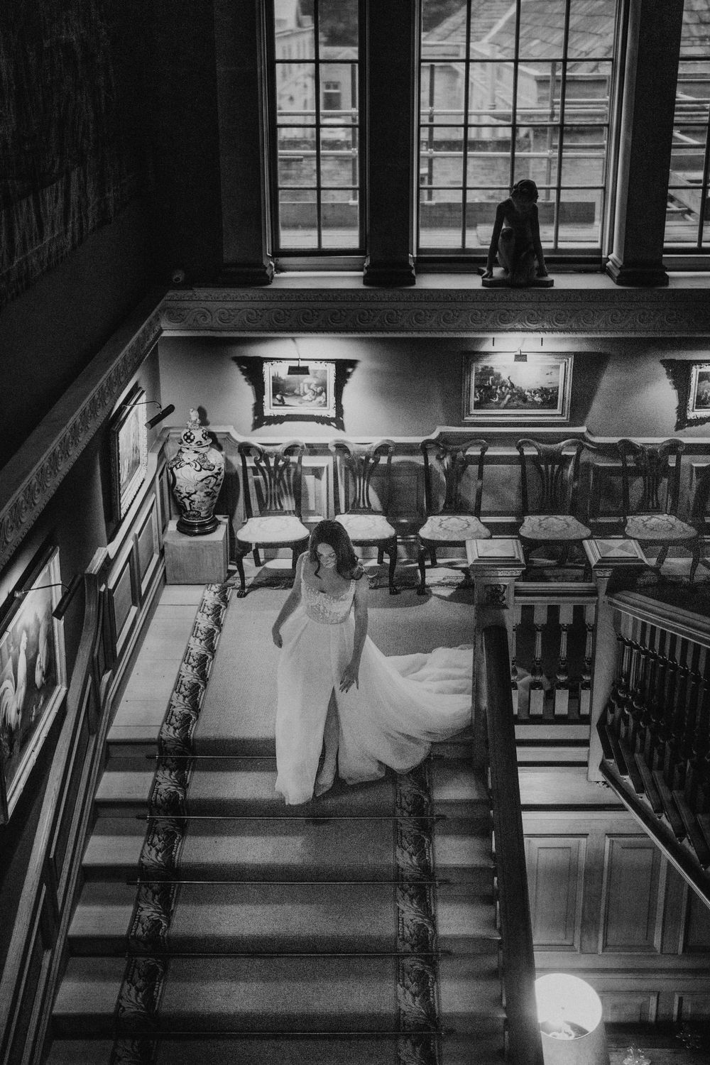 Artistic black and white photo of a couple in formal wear on vintage library stairs.
