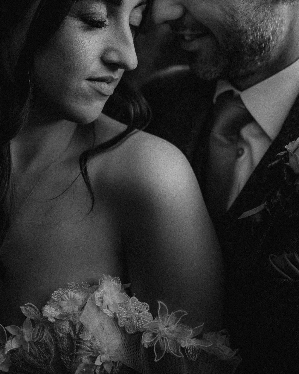 Intimate black and white portrait of a couple in formal attire with delicate floral details.