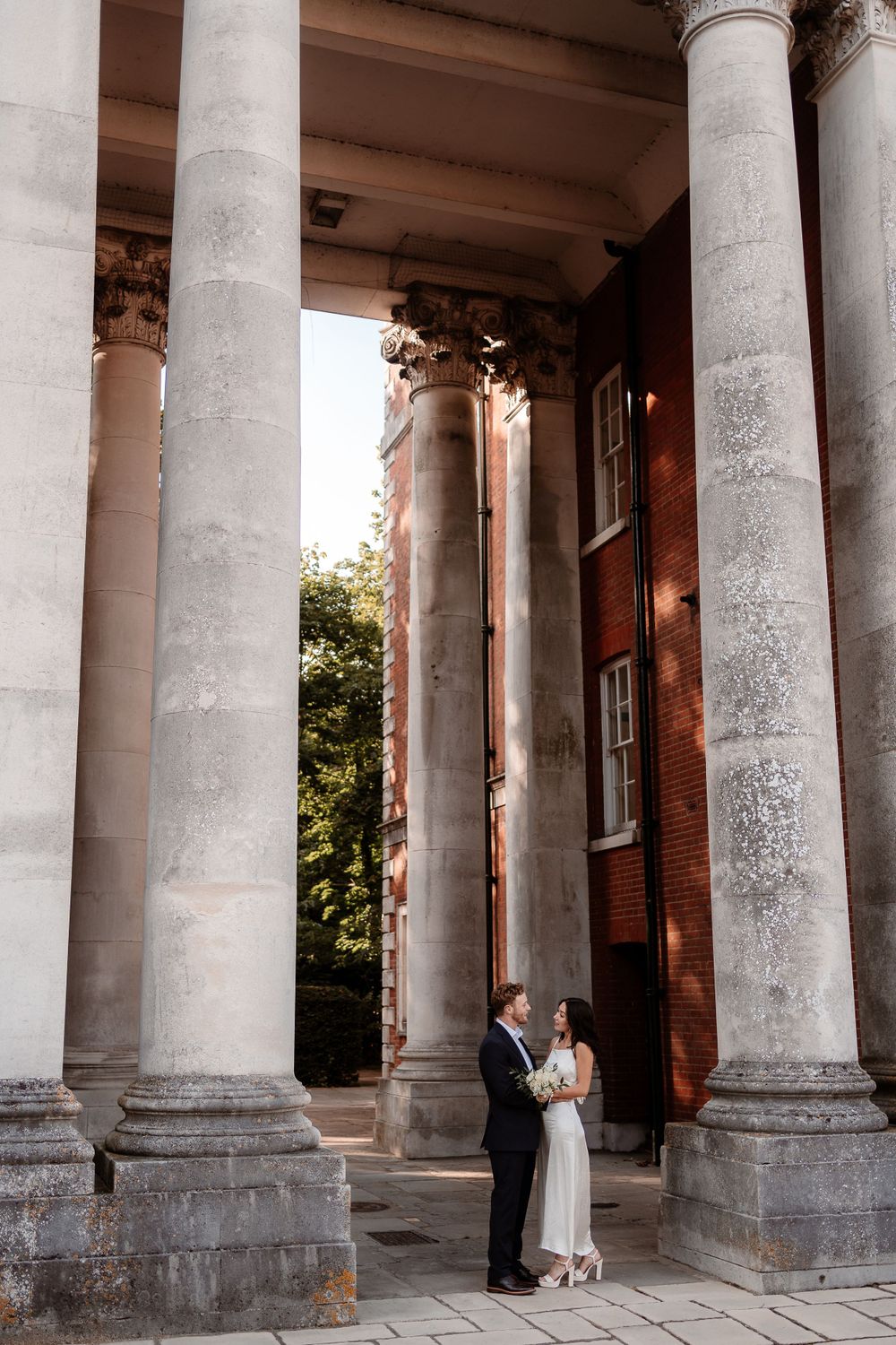 A wedding couple poses between grand stone columns of a historic building.