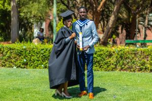 Two people share a joyful moment on a green lawn during graduation celebration, with one wearing academic regalia.