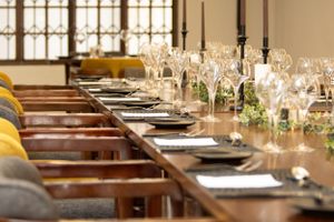 Long dining table set with elegant place settings, wine glasses, and candles in a rustic restaurant interior.
