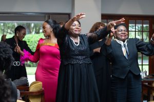 A group of people dancing and celebrating joyfully at a social gathering, with some wearing formal attire.