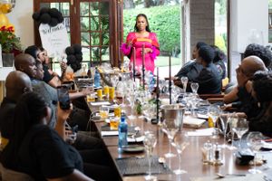 A person in a bright pink dress stands at the head of an elegant dinner table during a gathering at a restaurant.