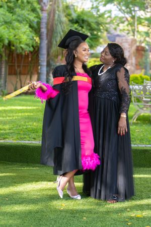 A graduation celebration in a garden setting features vibrant pink and black formal attire and mortarboard cap.