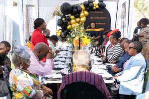 People gathered around an elegantly decorated table with black and gold balloon arrangements for a celebration.
