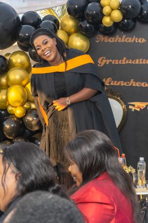 A graduation celebration setup with black and gold balloon decorations and banquet tables in the background.