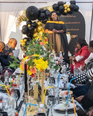 Elegant event setup with black and gold balloon arch decorations, festive table settings and colorful floral centerpieces.