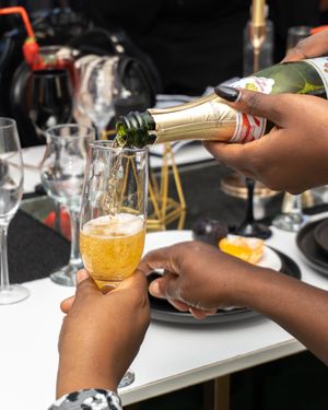 Hands pouring golden champagne into a glass during a celebratory dining setting with plates and table decor.