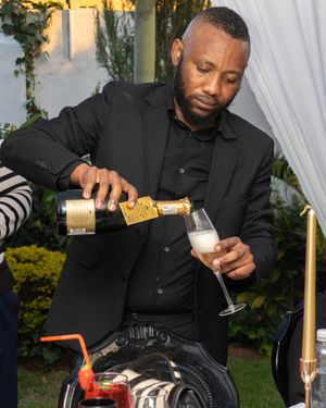 Professional bartender in black attire carefully pours champagne into a glass at an outdoor event.
