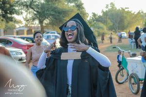 Graduate in cap and gown celebrates joyfully outside during graduation ceremony on sunny day.