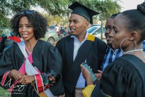 Graduates in black caps and gowns celebrate together during an outdoor commencement ceremony.
