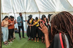 Group gathered inside a white tent during what appears to be a graduation celebration with casual and formal attire.