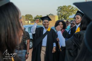 Graduates in black caps and gowns share joyous laughter during an outdoor graduation celebration.