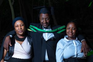 Three people pose together for a graduation photo wearing casual and formal attire with green accents.