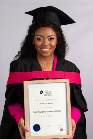 Graduate in black and pink academic regalia displays certificate from Property Institute.