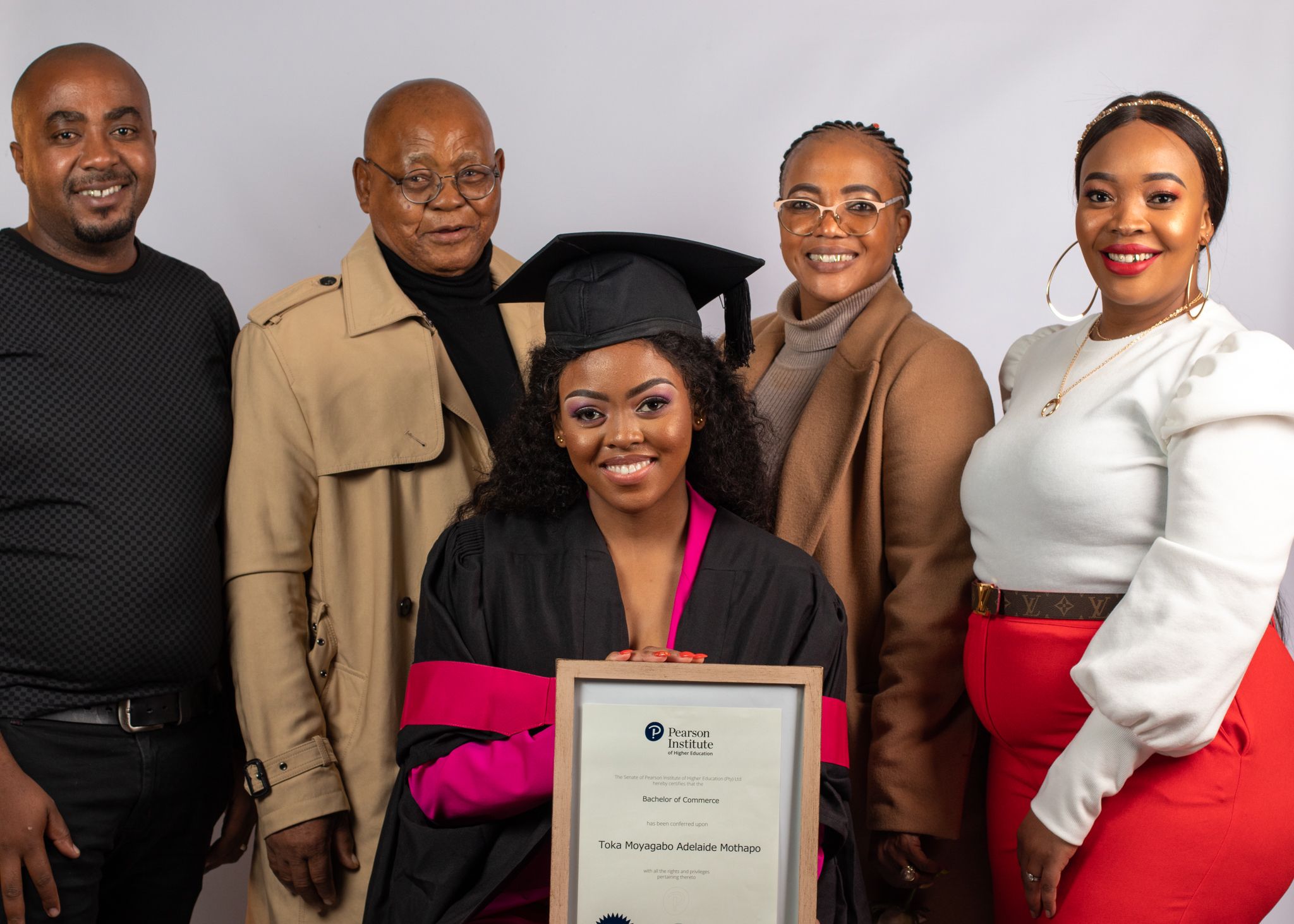 Group photo showing graduate in academic regalia surrounded by family members at graduation ceremony.