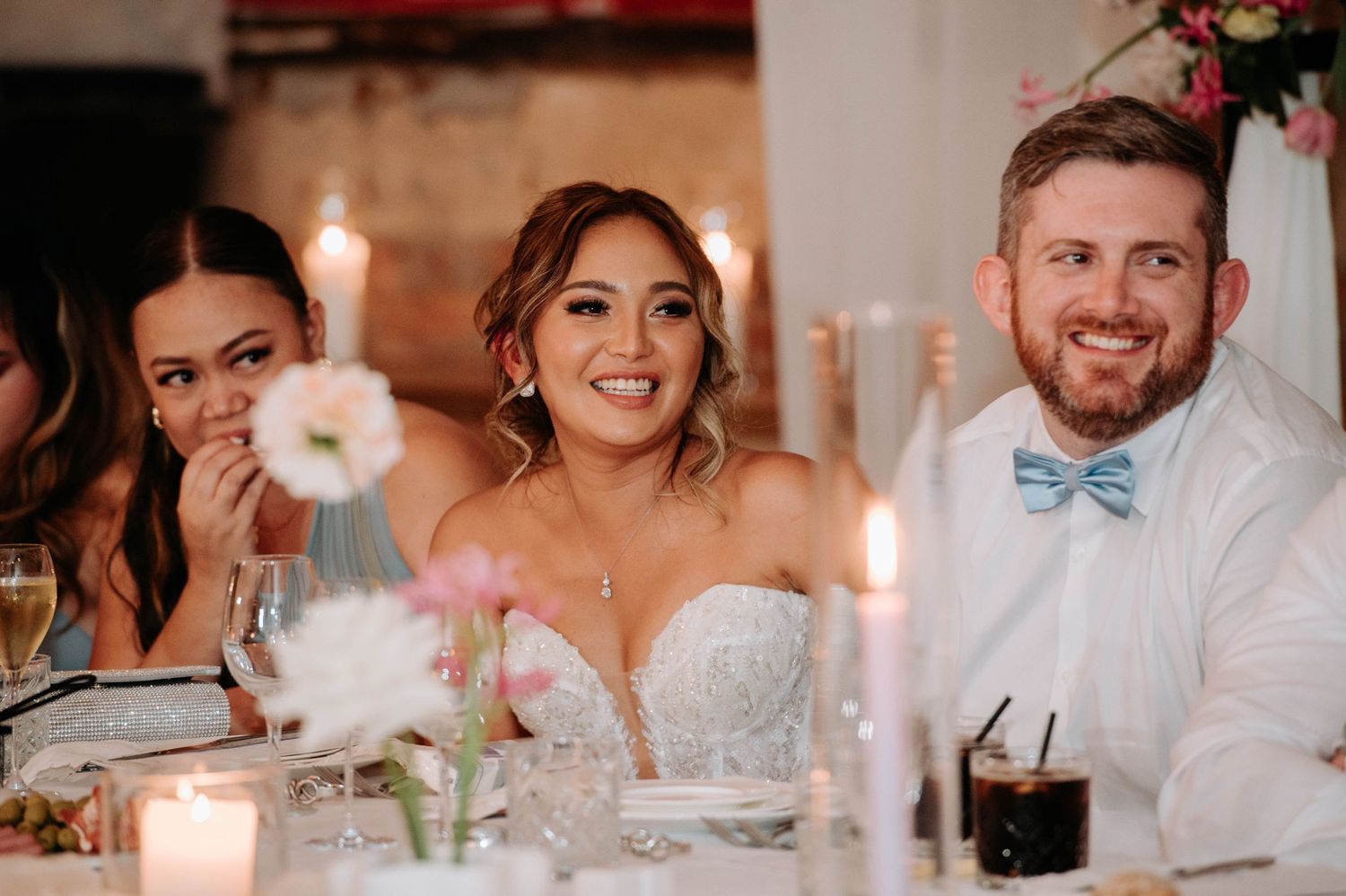 Wedding reception dinner with elegant table settings and candlelight in a rustic brick venue.