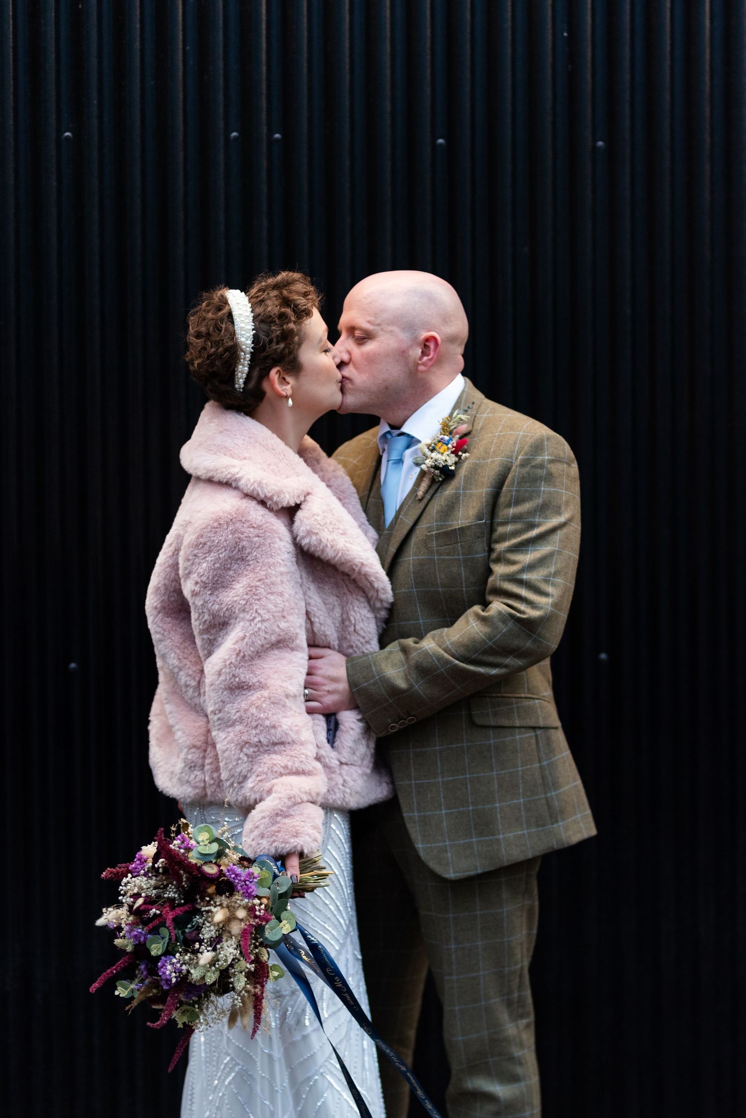 Wedding couple sharing a romantic moment against a dark background with vibrant floral bouquet.