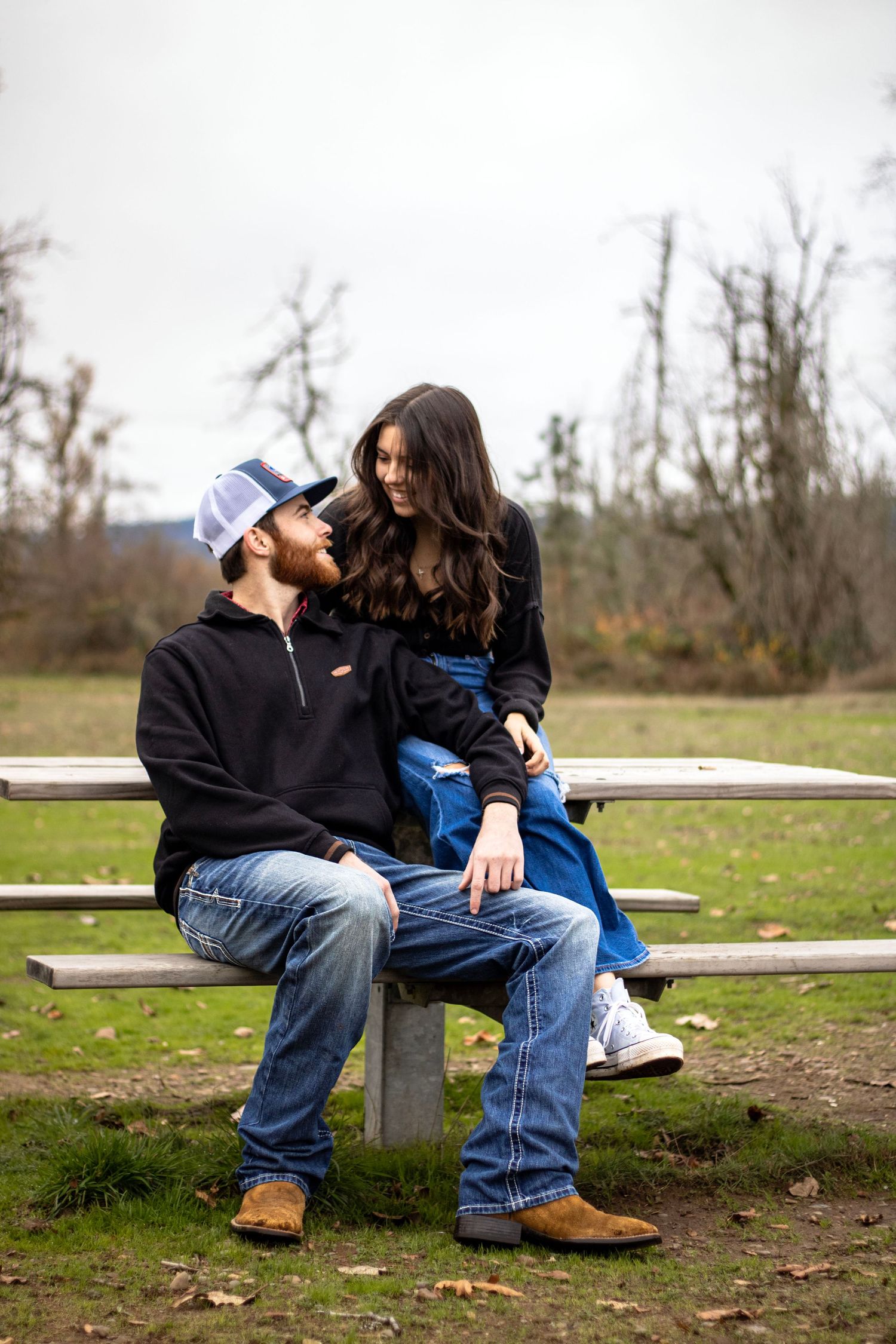 man and woman sit at picnic table, his elbow is on her knee and they smile at each other