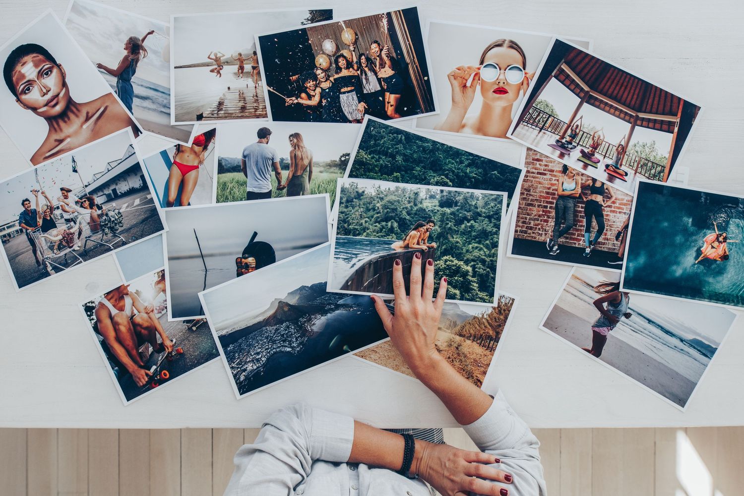 Personal travel photographs arranged on a light wooden table with a person's hand reaching to organize them.