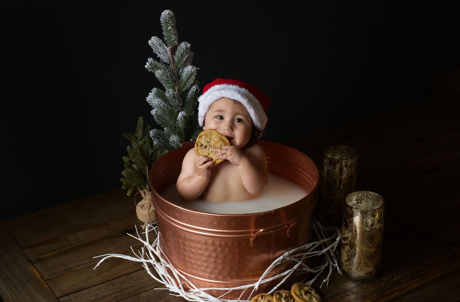 Baby in Santa hat sitting in copper bath tub with holiday decorations.