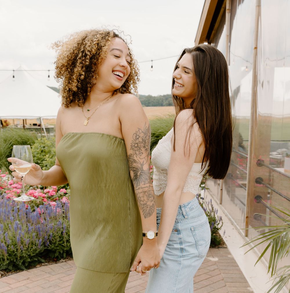 Two friends share a joyful moment in front of a flower garden.
