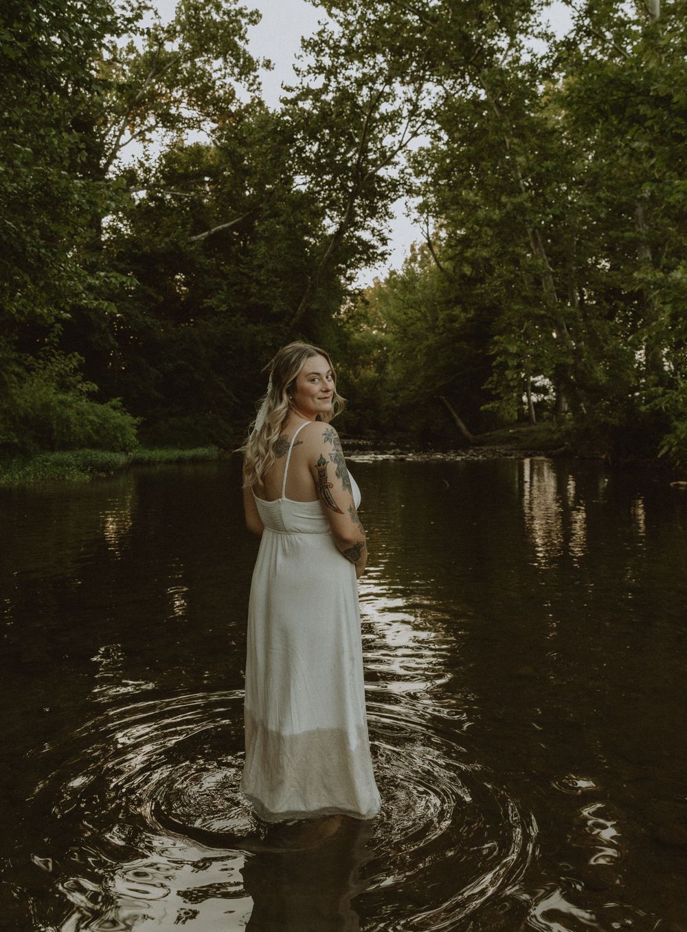 Atmospheric portrait of person in white dress standing in tranquil lake water.