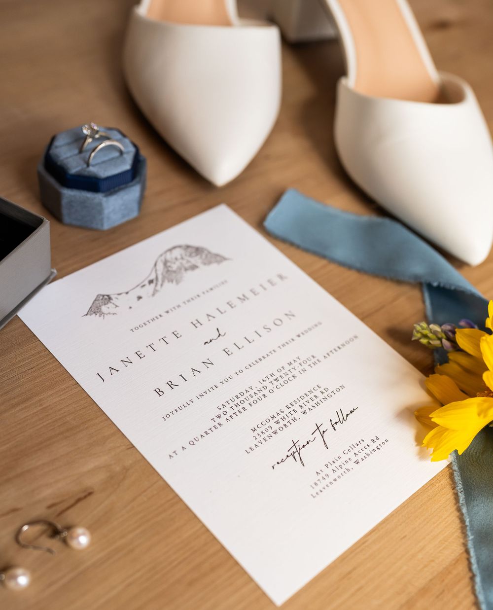 Wedding invitation with white heels and blue details on wooden surface.