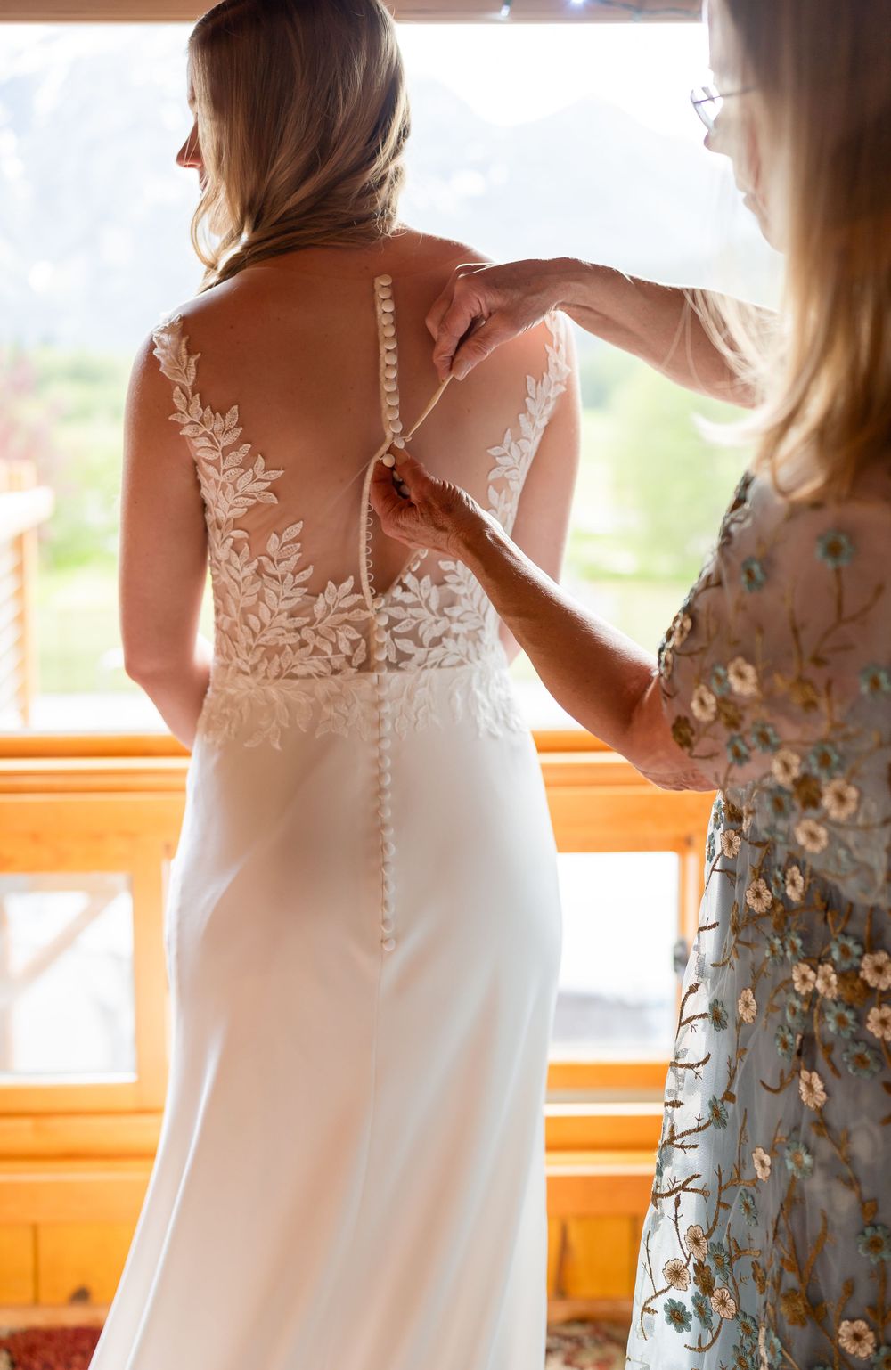 Close-up of intricate lace detail on back of wedding dress being buttoned.