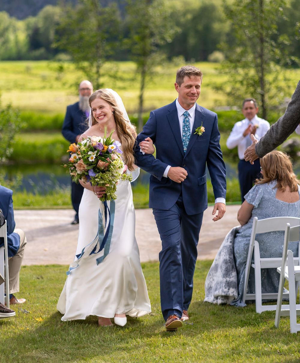 Joyful wedding exit along garden path with colorful bouquet.