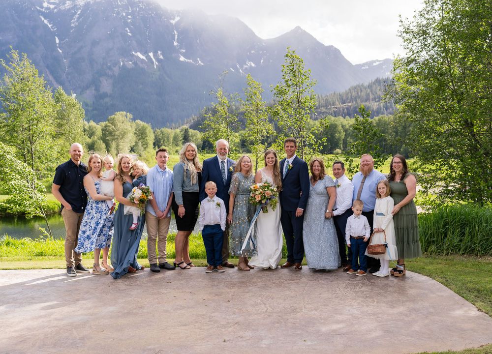 Wedding party group photo with mountain backdrop in natural outdoor setting.