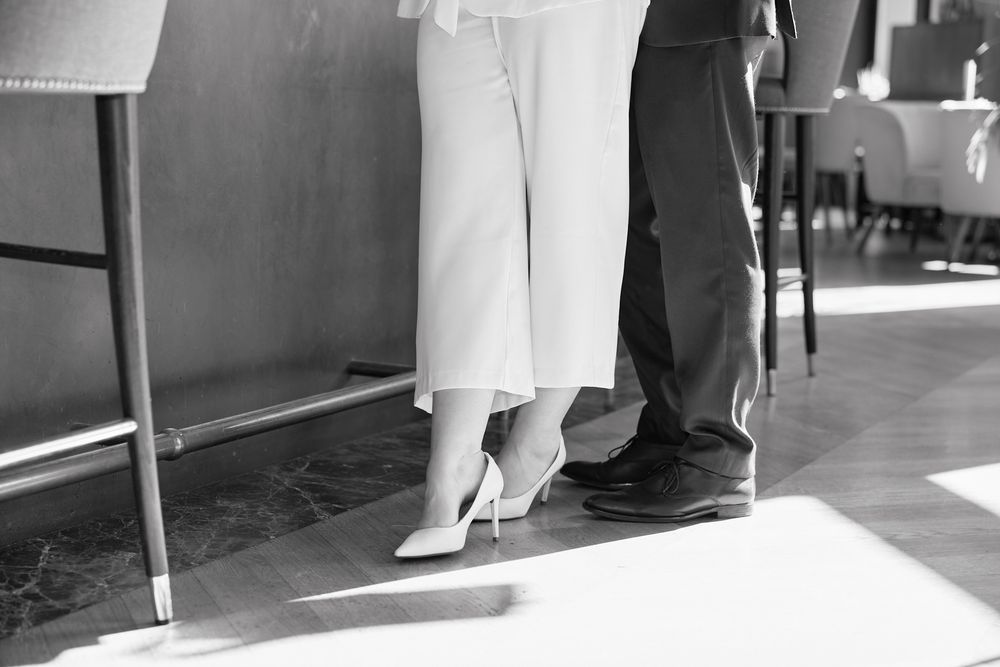 Black and white photo showing feet of people waiting in line against a sunlit wall.