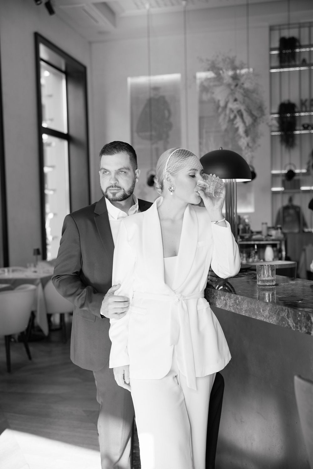 An elegant black and white photo of a couple in formal attire standing in a modern interior space.