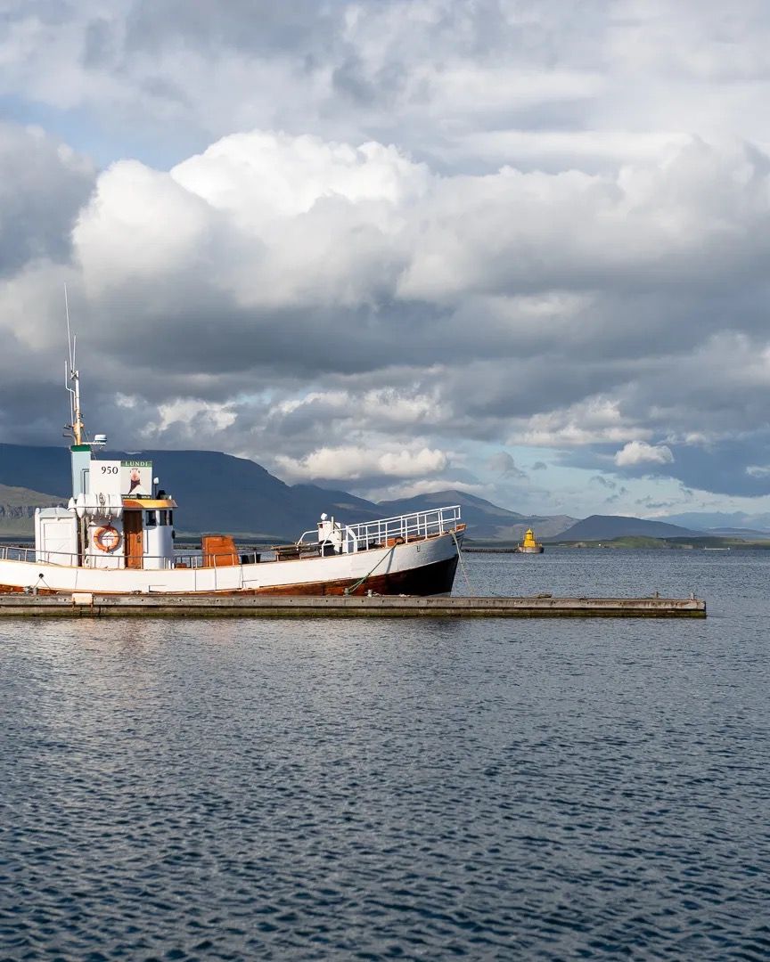 Cargo ship docked beside a harbour wall under dramatic cloudy skies.