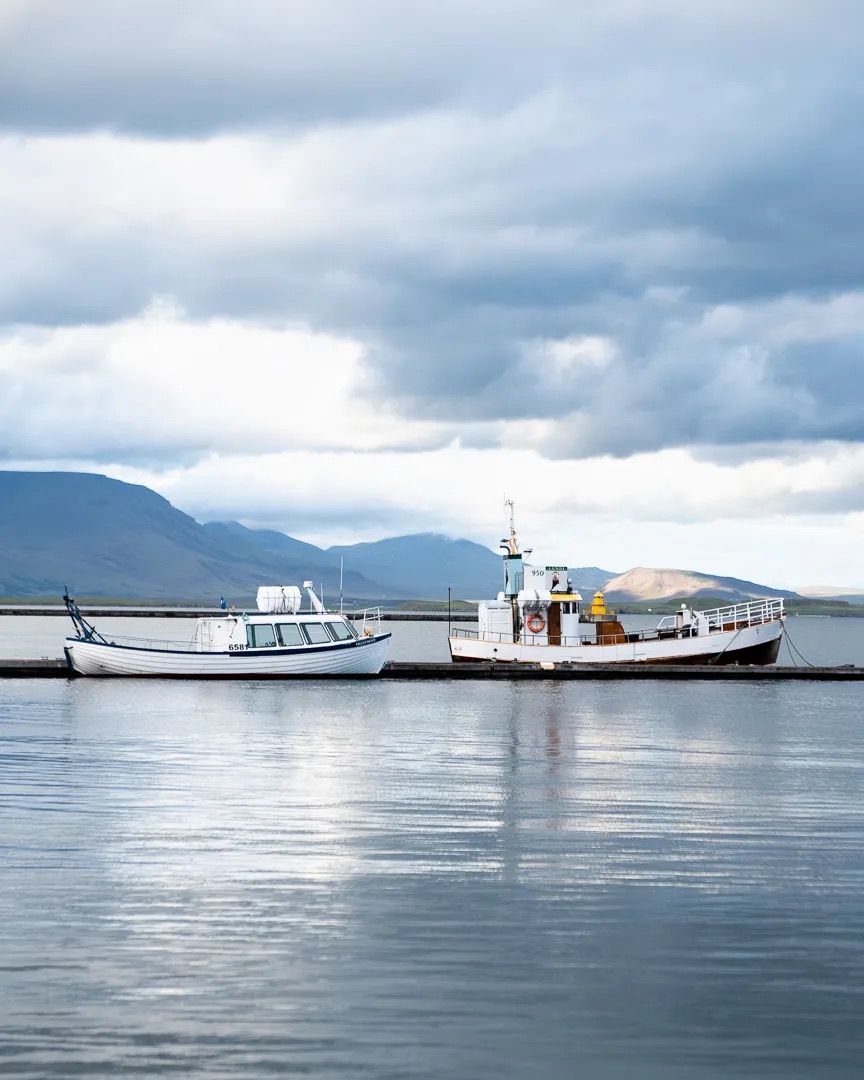 White boat on still blue water with mountains and clouds in the distance.